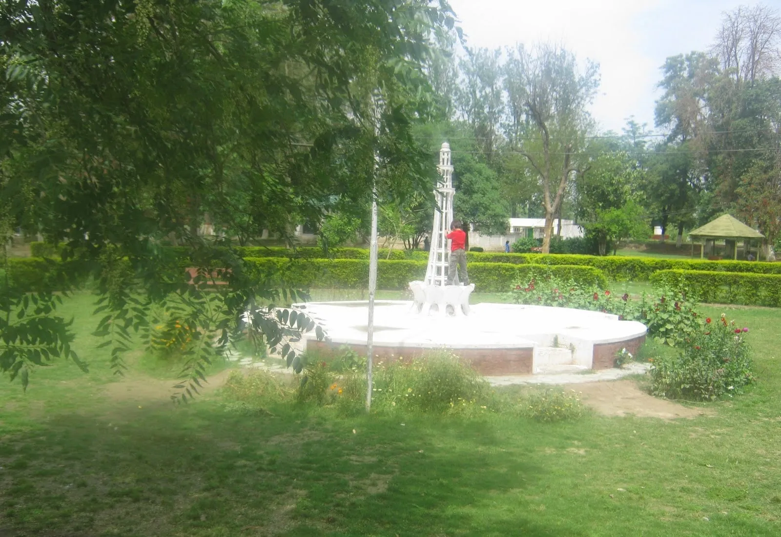 The white monument and fountain circle at the heart of the forest park, surrounded by hedged gardens with a pagoda hut behind